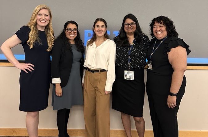Five presenters stand and pose at the front of a lecture hall.